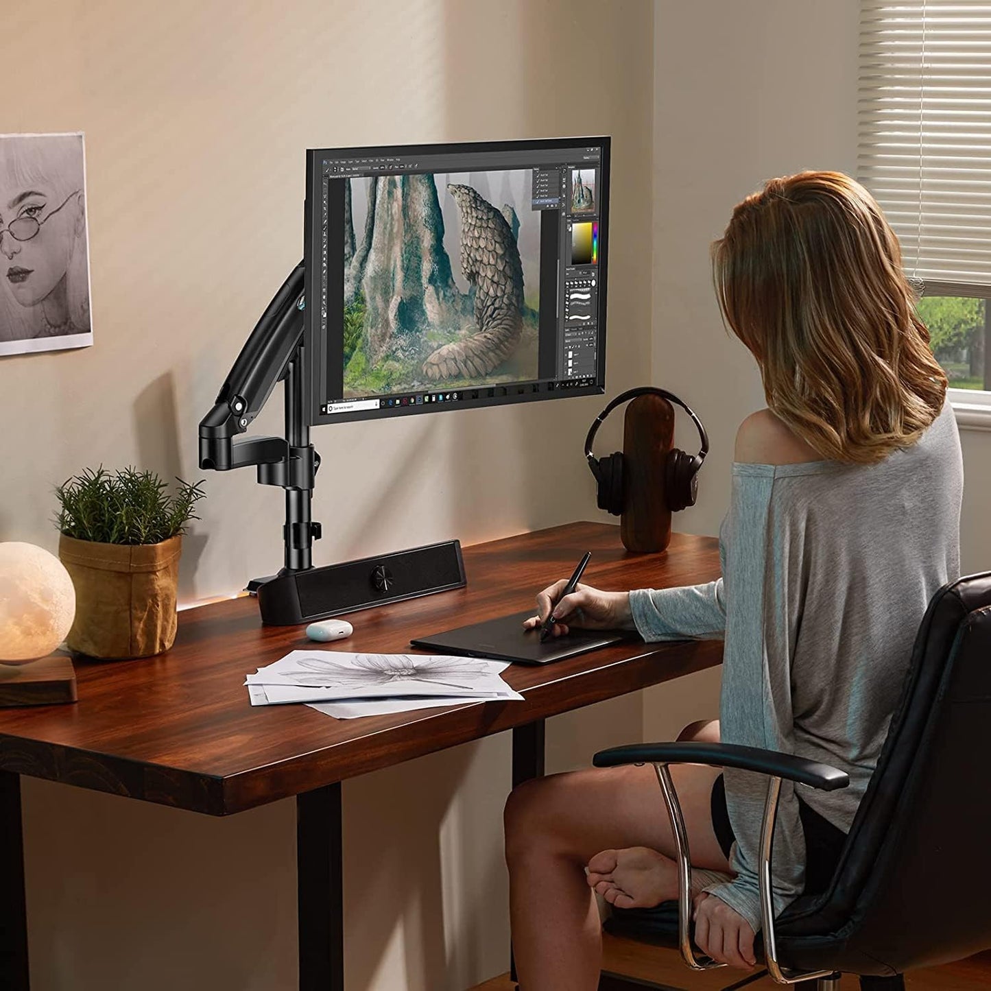 Woman sketching at desk with HUANUO monitor mount supporting a screen displaying mountain view.